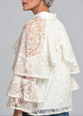 A woman shown from the back wearing a cream lace ruffled blouse against a solid gray studio background.