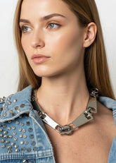 Woman wearing a denim jacket with studded details and a metallic necklace against a plain background