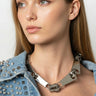 Woman wearing a denim jacket with studded details and a metallic necklace against a plain background
