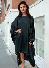 Woman wearing a black dress with a cape-like design on a city street.